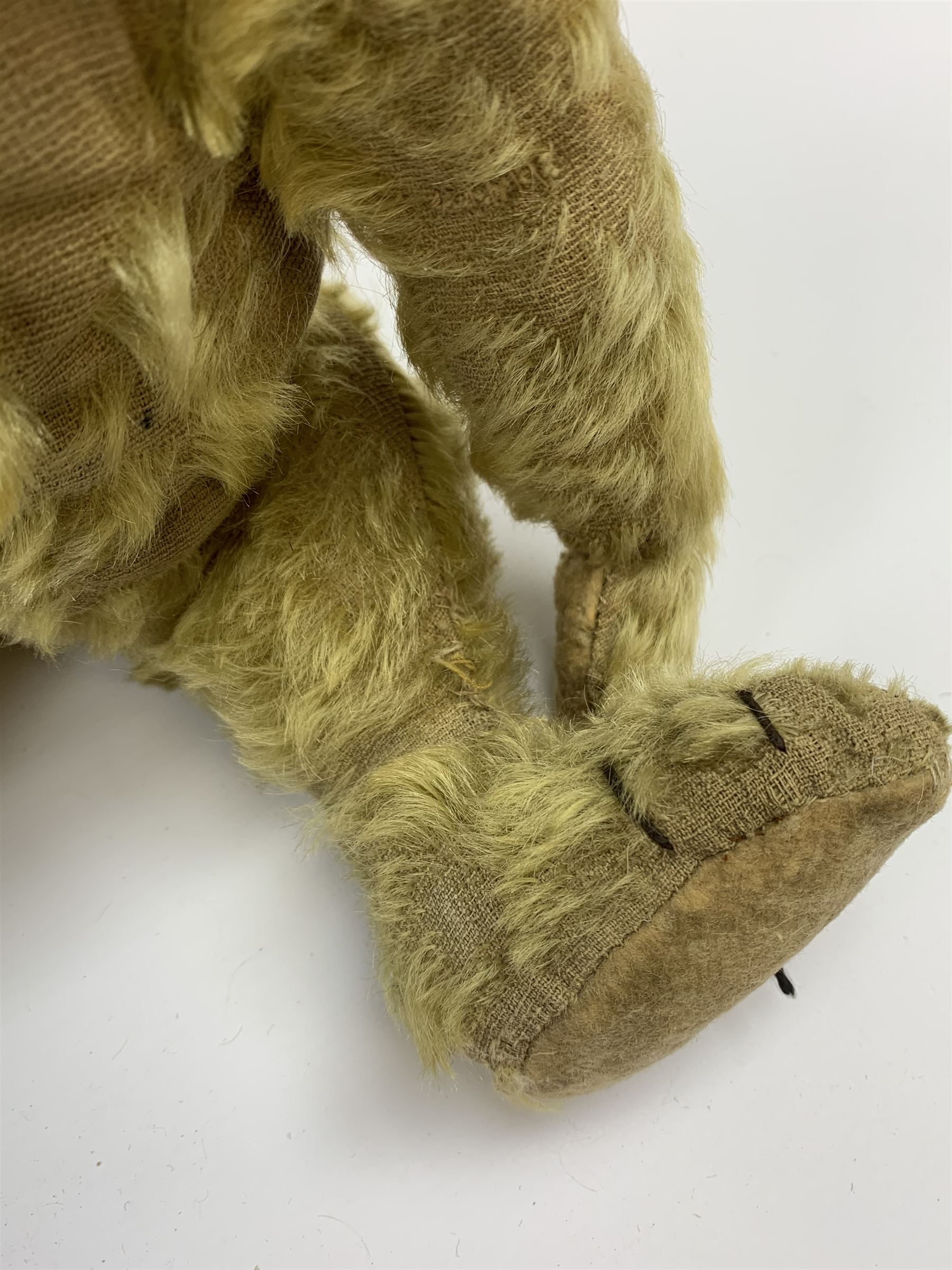Early 20th century English teddy bear, with wood wool filled body with jointed limbs, felt covered paw pads, five claw stitching to feet and elongated arms with spoon shaped paws H14