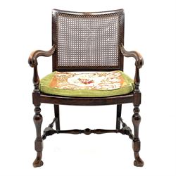 Early 20th century beech framed armchair, curved caned back and seat, down swept moulded arms on turned supports terminating with scrolled feet, turned stretchers, with needle work and green fabric seat cushion 