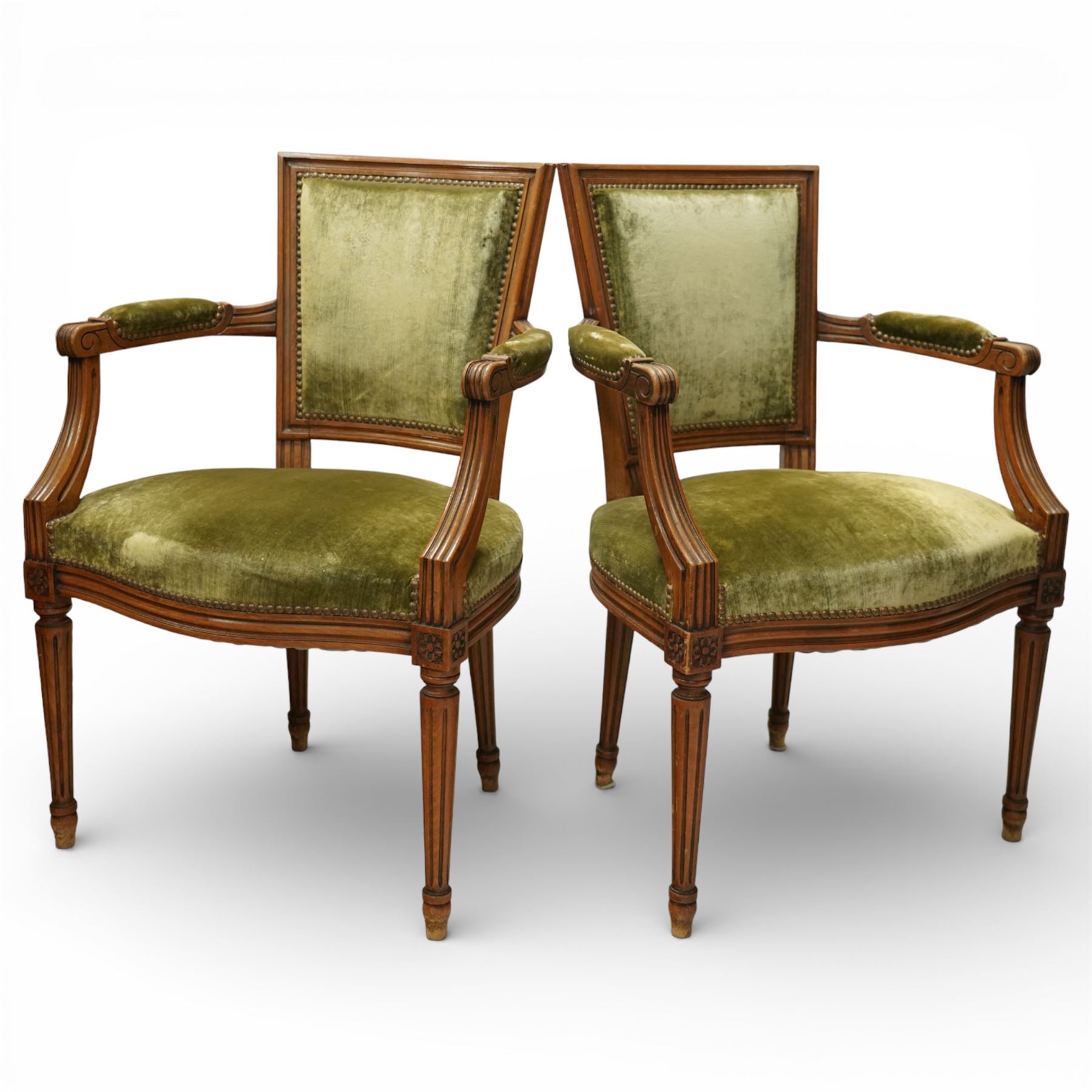 French Louis XVI style walnut armchairs, rectangular upholstered backs with nailhead trim, padded seats upholstered en suite, out-swept arms with upholstered pads, fluted supports with carved rosettes to the knees, on turned and fluted tapering legs
