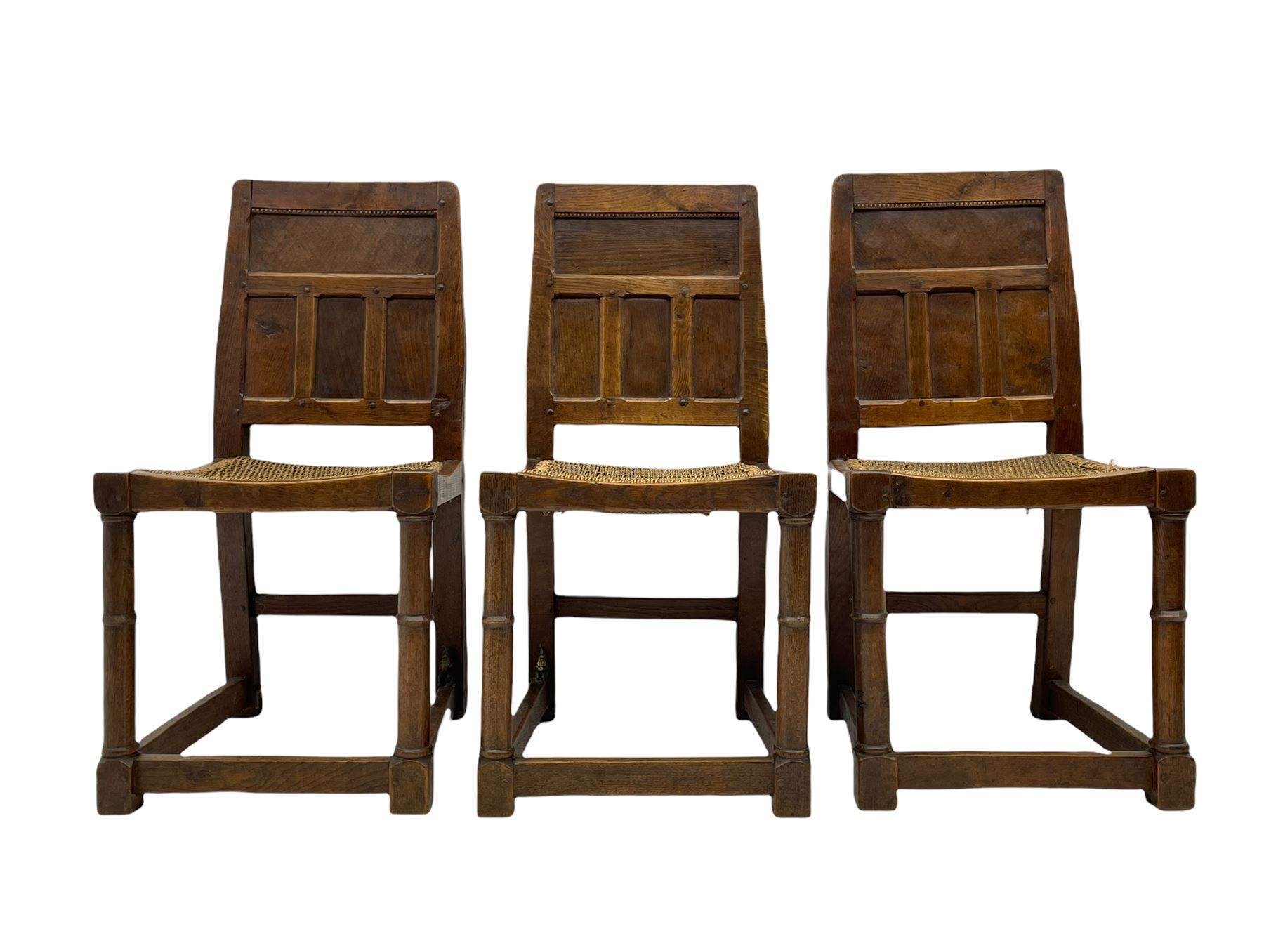 'Gnomeman' set of three oak dining chairs, panelled backs over curved seat rails with drop in rope rush seats, turned front supports with collar joined by plain stretchers, two with carved seated gnome figures, painted

Provenance - This collection of early 'Gnomeman' furniture comes to us directly from the Whittaker family. The pieces were made by the vendor's father Thomas Whittaker in the 1930/40s for his own use. During this time, he lived in York and made items for himself and friends. Whittaker adopted the gnome as a signature and trademark after his move to Littlebeck, Whitby.
