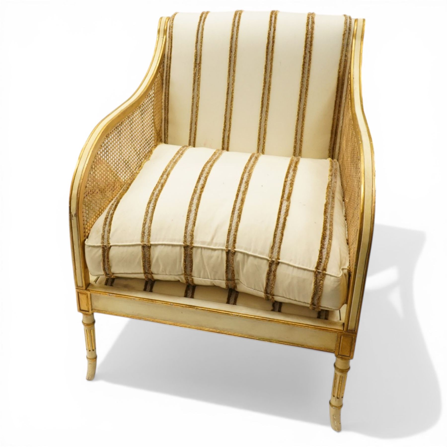 Louis XV design cream painted and parcel-gilt bergere armchair of large proportions, high scrolled back over canework arms, upholstered in striped fabric with over-stuffed loose seat cushion, on fluted supports