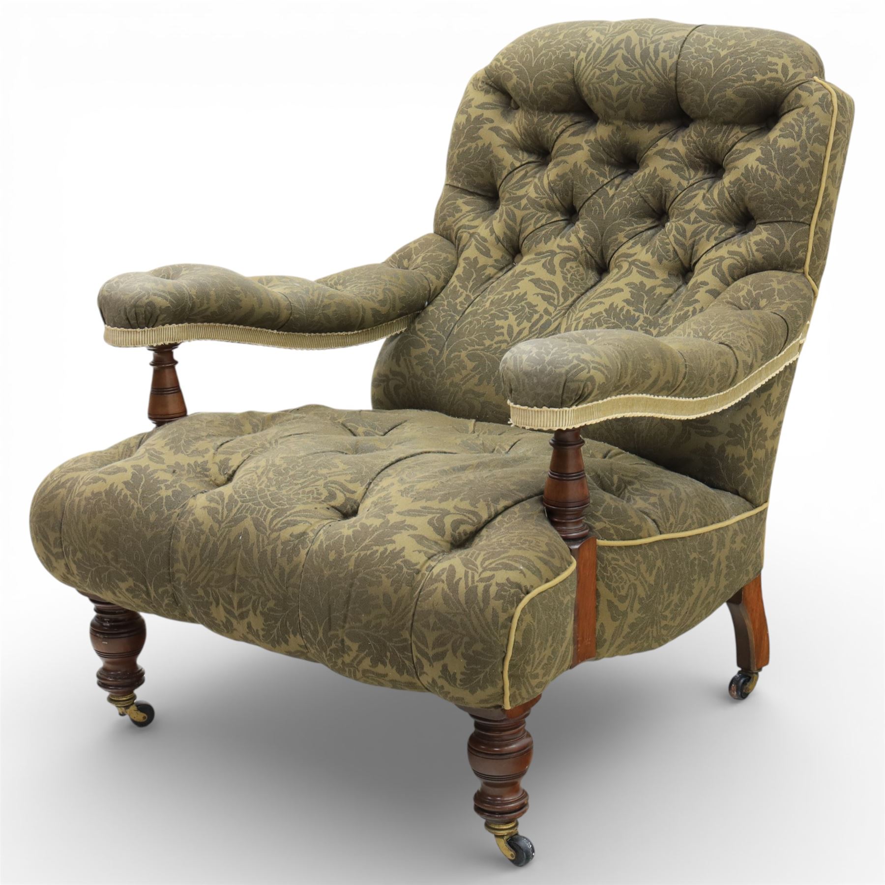 Late Victorian open armchair, in the manner of Howard & Sons, with deep buttoned seat and back upholstered in green damask fabric, with fringed detail to the lower arms, raised upon turned front legs with brass castors