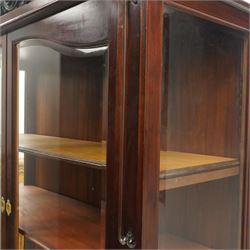 Large and impressive 19th century heavily carved mahogany display cabinet, the ornate pediment carved with a central scalloped and foliate rocaille motif with extending acanthus leaves and egg-and-dart moulding flanked by acanthi finials, over a central cartouche with carved bow-and-arrow motif and trailing scrollwork, the bookcase enclosed by two glazed doors with bevelled glass sides, the base with a gadrooned upper edge over a central rocaille ornament with scrolling acanthus leaves, the panelled frieze with further foliate motifs, raised on large carved snarling lion mask supports with floral garlands and claw feet, united by a concave rectangular platform base with gadrooning egg-and-dart moulding