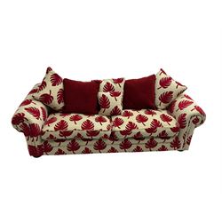 Large three seat sofa, upholstered in cream and red leaf patterned fabric with matching scatter cushions, raised on carved compressed bun feet
