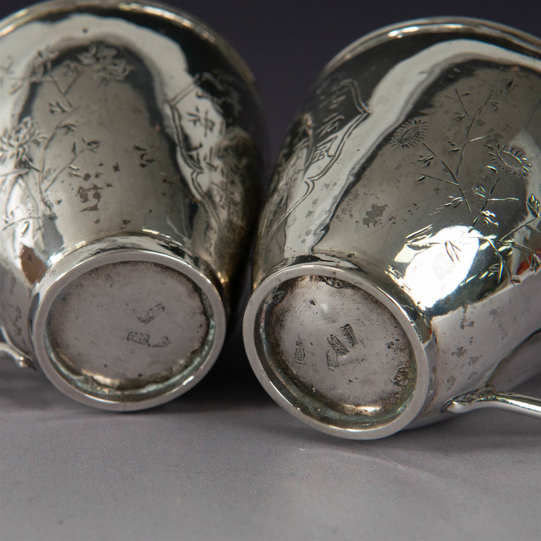 Pair of Chinese export silver teacups, both decorated with character marks, one with floral decoration, the other decorated with a bird within bamboo branches, both with indistinct maker's marks beneath, H6cm