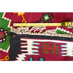 Persian Fars province crimson ground kilim rug, decorated with two rows of geometric emerald green motifs containing stylised plant designs, enclosed by an ivory and dark indigo guard band