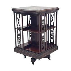Edwardian inlaid mahogany revolving bookcase, shaped square moulded top with central motif and satinwood band, two tiers with pierced vertical splats, on swivel action base with ceramic castors