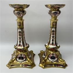 Pair of modern Royal Crown Derby Old Imari 1128 pattern candlesticks, each with shaped drip tray affixed to squat socket, upon spreading stem and canted square base with gilt dolphin edges, with printed marks beneath including Roman numeral year cypher for 2003, H26.5cm, with original boxes