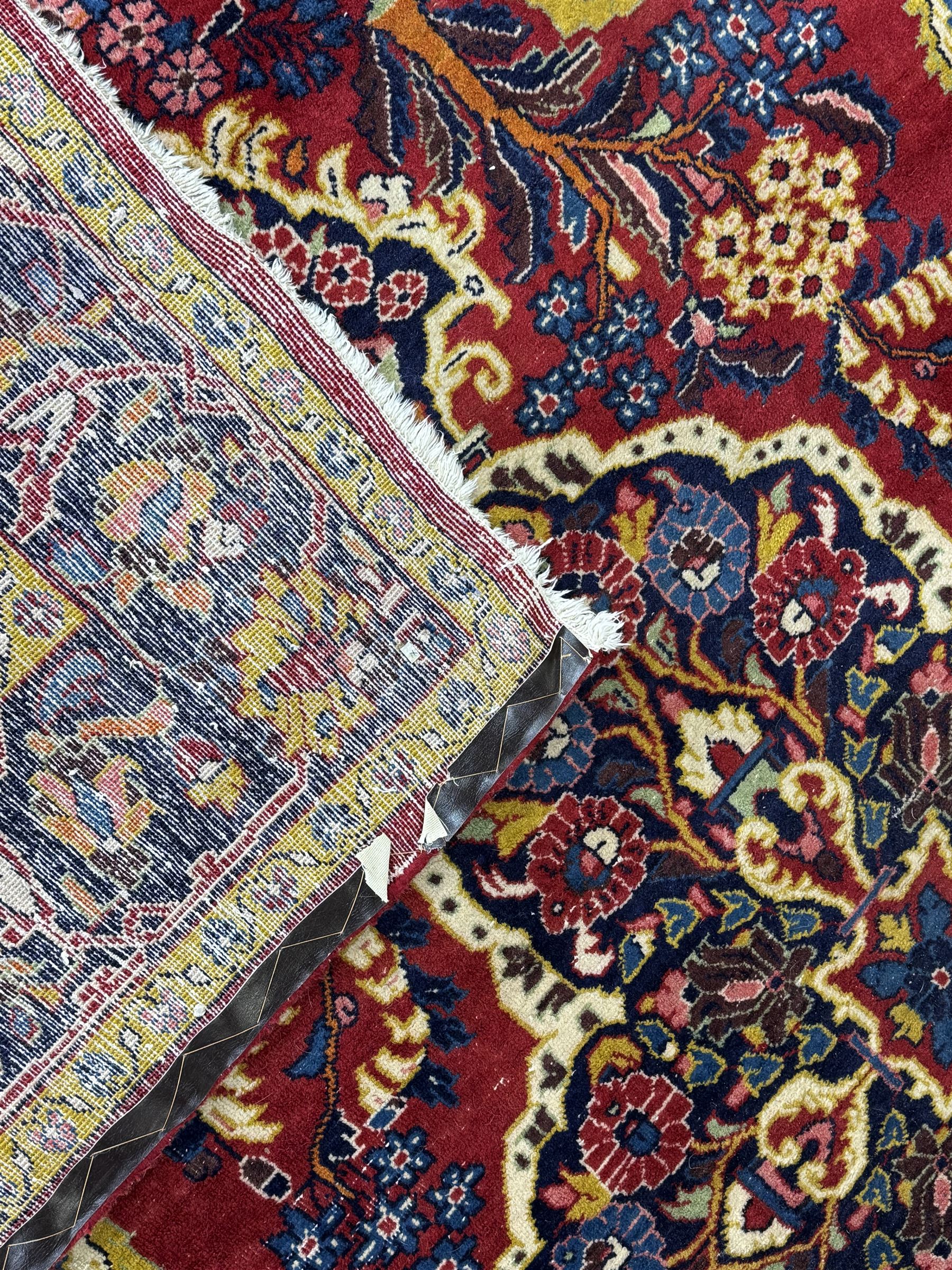 Mid-20th century Persian ground rug, featuring a bold red field and large lobed medallion, flanked by floral corner spandrels, enclosed within multiple borders of stylised vines and palmettes, with fringe to both ends