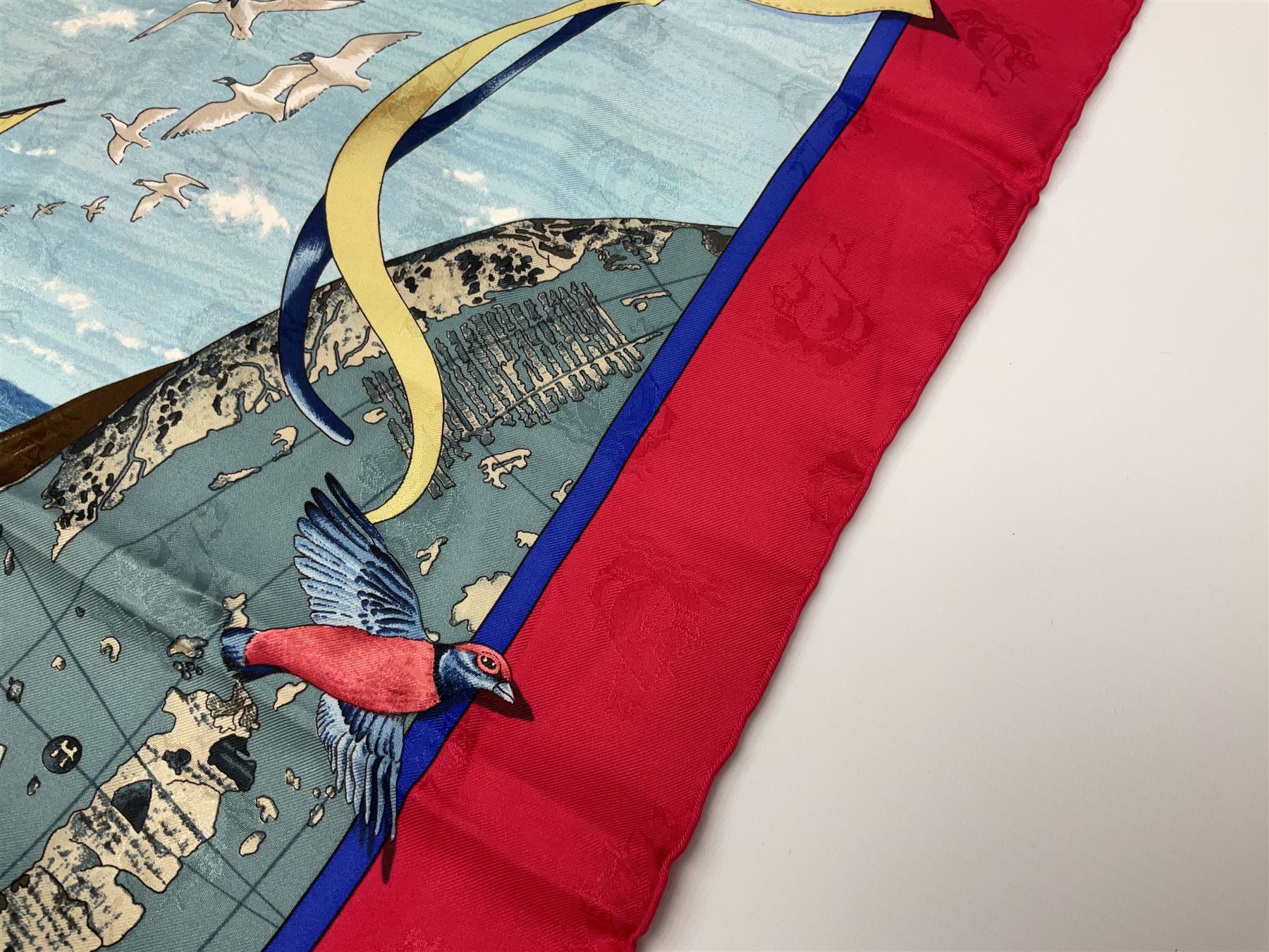Hermès 'Christophe Colomb Découvre l'Amérique' jacquard silk scarf, designed by Carl de Parcevaux in 1992, limited edition for the bi-centenary of the discovery of America, printed with a central image of Christopher Columbus' ship at sea, surrounded with colourful stylised feathers, birds, flags, globes, shells and flowers, contained within vibrant red border, with rolled hand stitched edges and Hermes material label, 87cm square