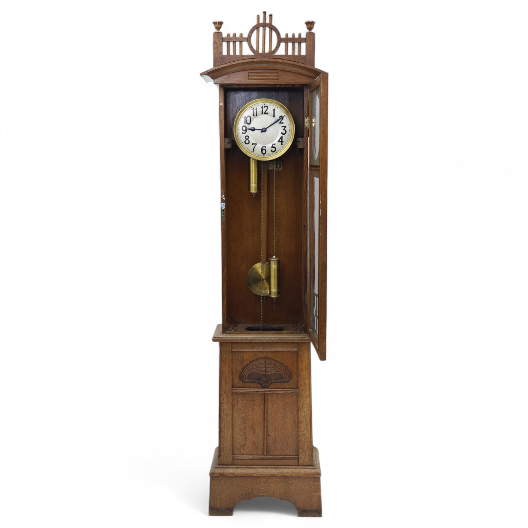 German-Art Deco 8-day longcase clock in an oak case, with a curved top and open fence work pediment, with reeded decoration and a fully glazed case door with a rectangular brass open work panel, on a tall rectangular plinth with a period  carved motif, circular slivered dial with Arabic numerals and spade hands, two train HAC (Hamburg and American Clock Company) weight driven movement, sounding the hours and half-hours on a coiled gong, with weights and pendulum.   