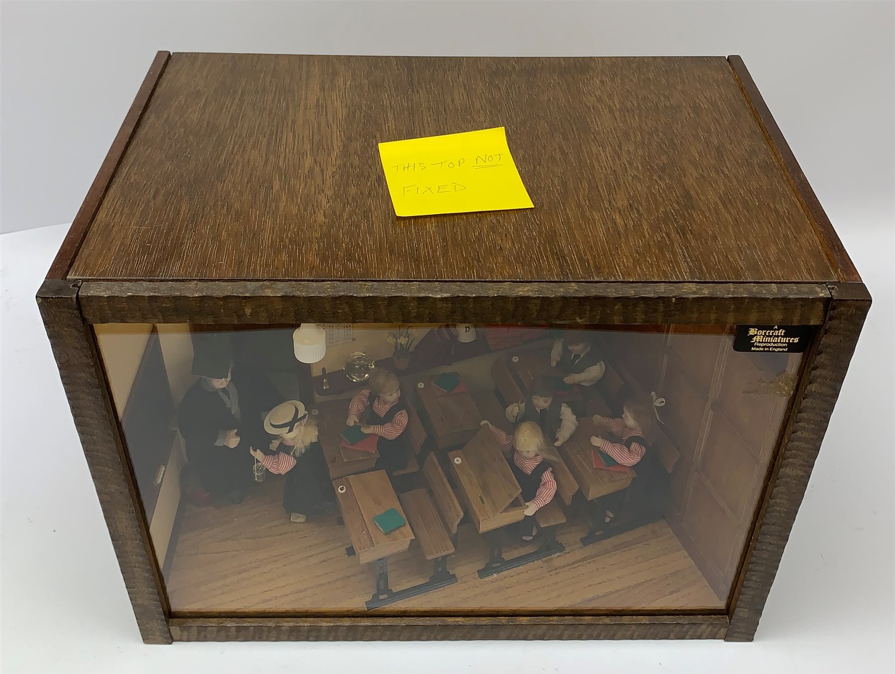 A 1/12th scale diorama of a school room interior, depicting pupils and teacher, the room furnished with panelled wall, desks, chalk board, globe, books and dunces hat, etc., H29cm L40cm D26cm.  
 
This model is based on a Victorian School Room in the museum in Armley, where the children and teachers would dress in period costume and attend lessons during the summer time.
