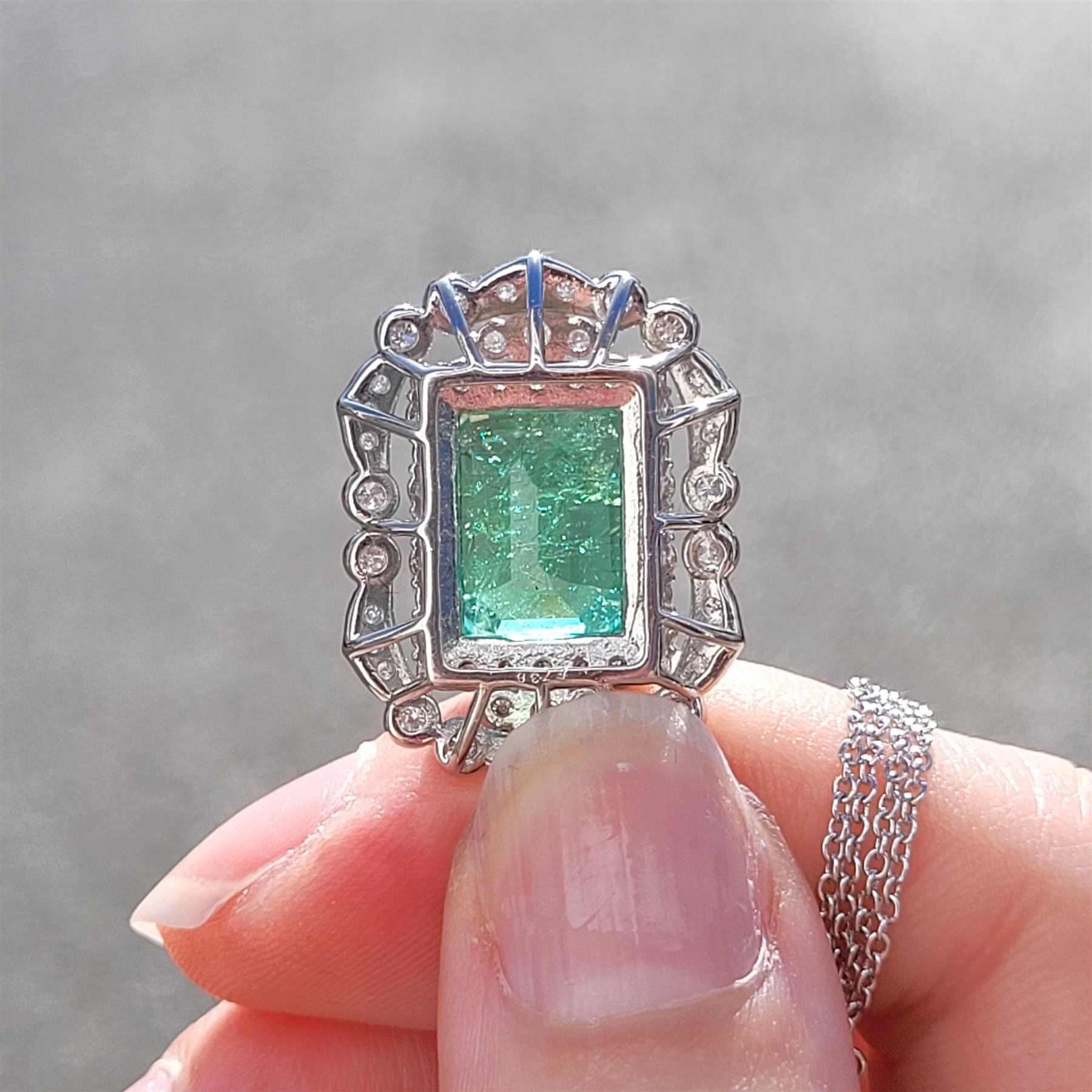 Platinum Colombian emerald and diamond pendant necklace, single octagonal cut emerald of 7.38 carat, surrounded by round cut diamonds in a fancy milgrain pierced design setting, stamped Pt 950, on a trace link chain necklace, total diamond weight 1.14 carat, with GCS certificate