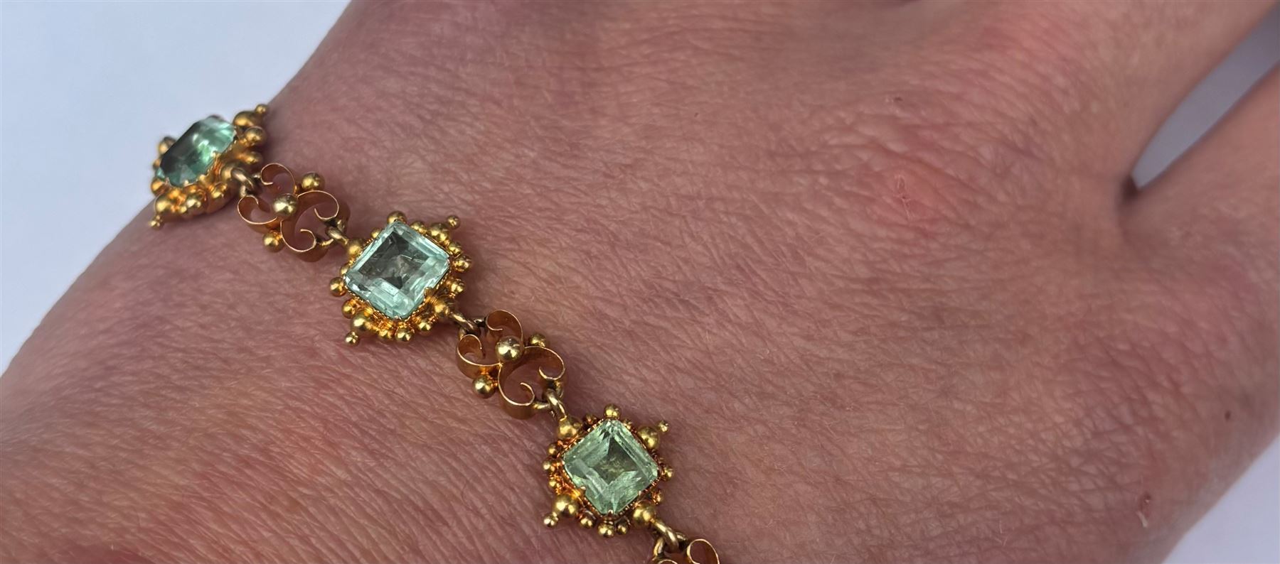 19th century gold emerald necklace, seven closed back octagonal cut and square cut emeralds, surrounded by a fancy bead setting, each spaced by a pierced scroll and bead design link, to a cable link chain necklace, with The Gem & Pearl Laboratory report