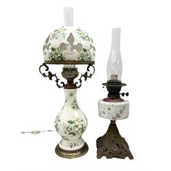 Two Victorian oil lamps, comprising larger example with transfer floral decoration on white ground with pierced domed shade and gilt fixtures upon baluster central stem, H66cm, and smaller painted with floral decoration on ornate base, both with glass chimneys
