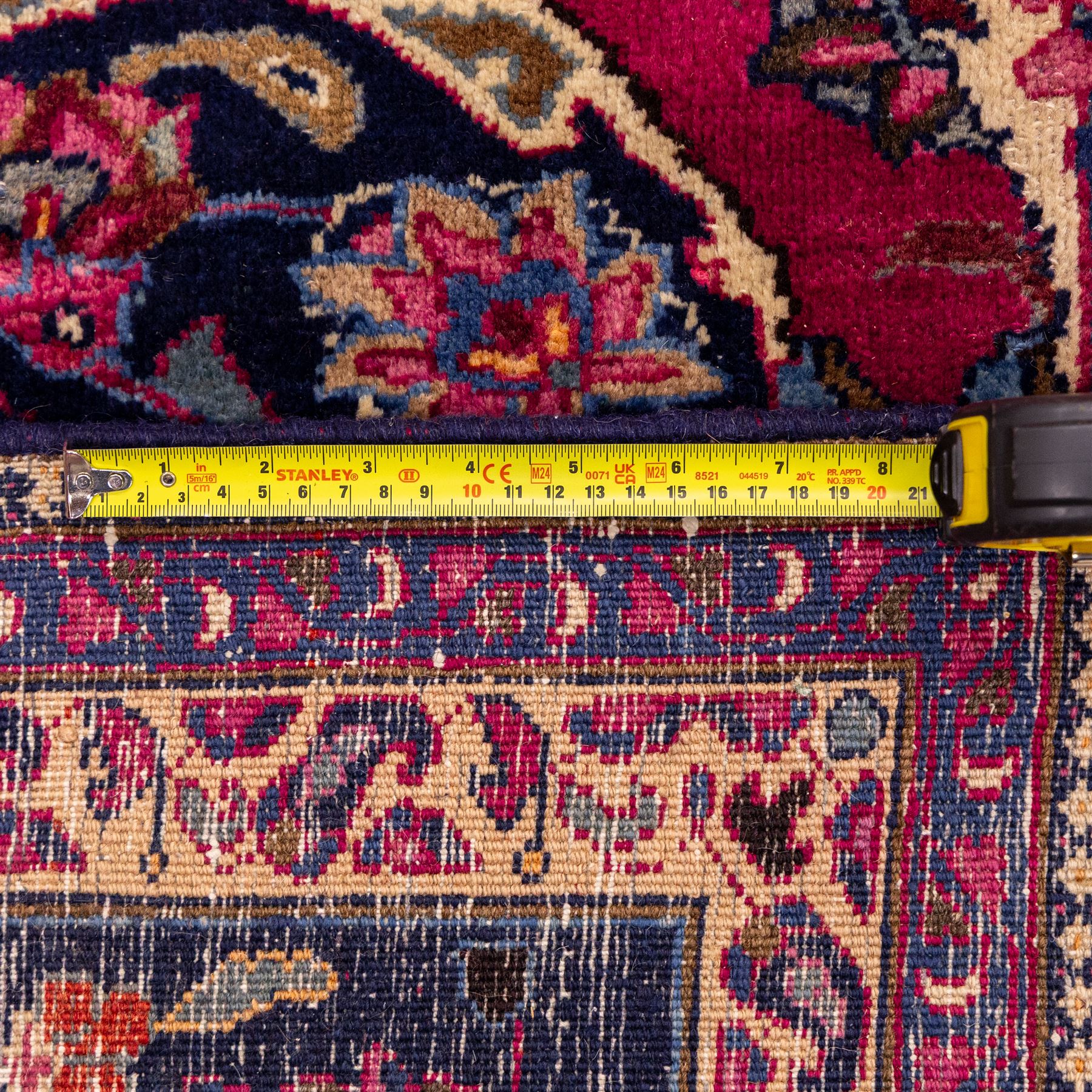 North East Persian Mashad hand-knotted carpet, rich madder red field with central cusped foliate medallion with issuing scrolling arabesques, palmettes, and floral sprays, enclosed within a broad indigo main border of bold palmettes, between multiple guard stripes, with cotton fringe ends 