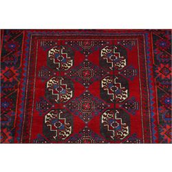 North East Persian Balochi hand-knotted runner, crimson field decorated with three vertical columns of repeating octagonal guls, each enclosing angular geometric motifs in deep indigo, ivory, and soft brown tones, guls linked by stepped diamond and cruciform devices, main border of stylized geometric floral motifs and angular vines, flanked by multiple guard borders, with cotton fringe ends 