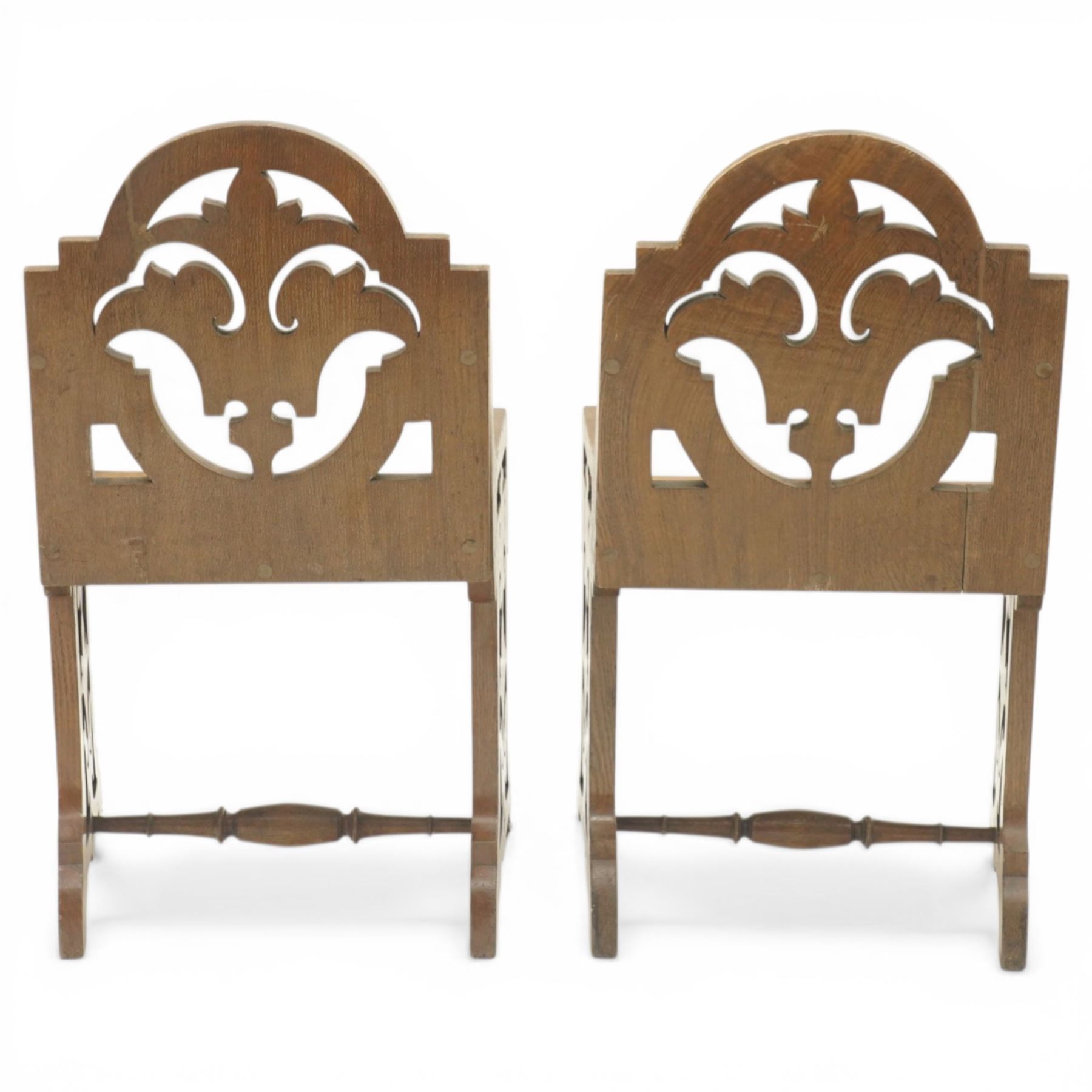 Gothic Revival oak ecclesiastical chairs, shaped cresting rails over pierced foliate splat backs, plank seats above shaped and pierced friezes, raised on shaped end supports united by turned stretchers, on small brass castors