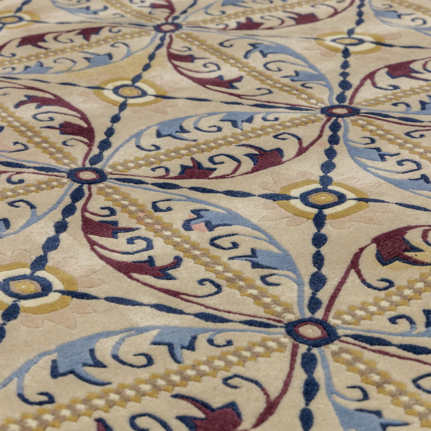 Rugs by Design - Nepalese wool rug, cream field decorated with repeating diamond trellis enclosing scrolling foliate motifs in blue, burgundy and ochre, within chain-link border and fringed ends