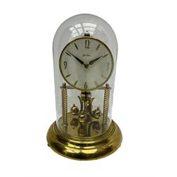 A mid-20th century “Bentima” 400-day anniversary torsion clock with a 7” circular brass base and unenclosed movement supported on two twisted columns, with a white dial gilt numerals and baton hands, four-ball rotary pendulum and glass dome. 

