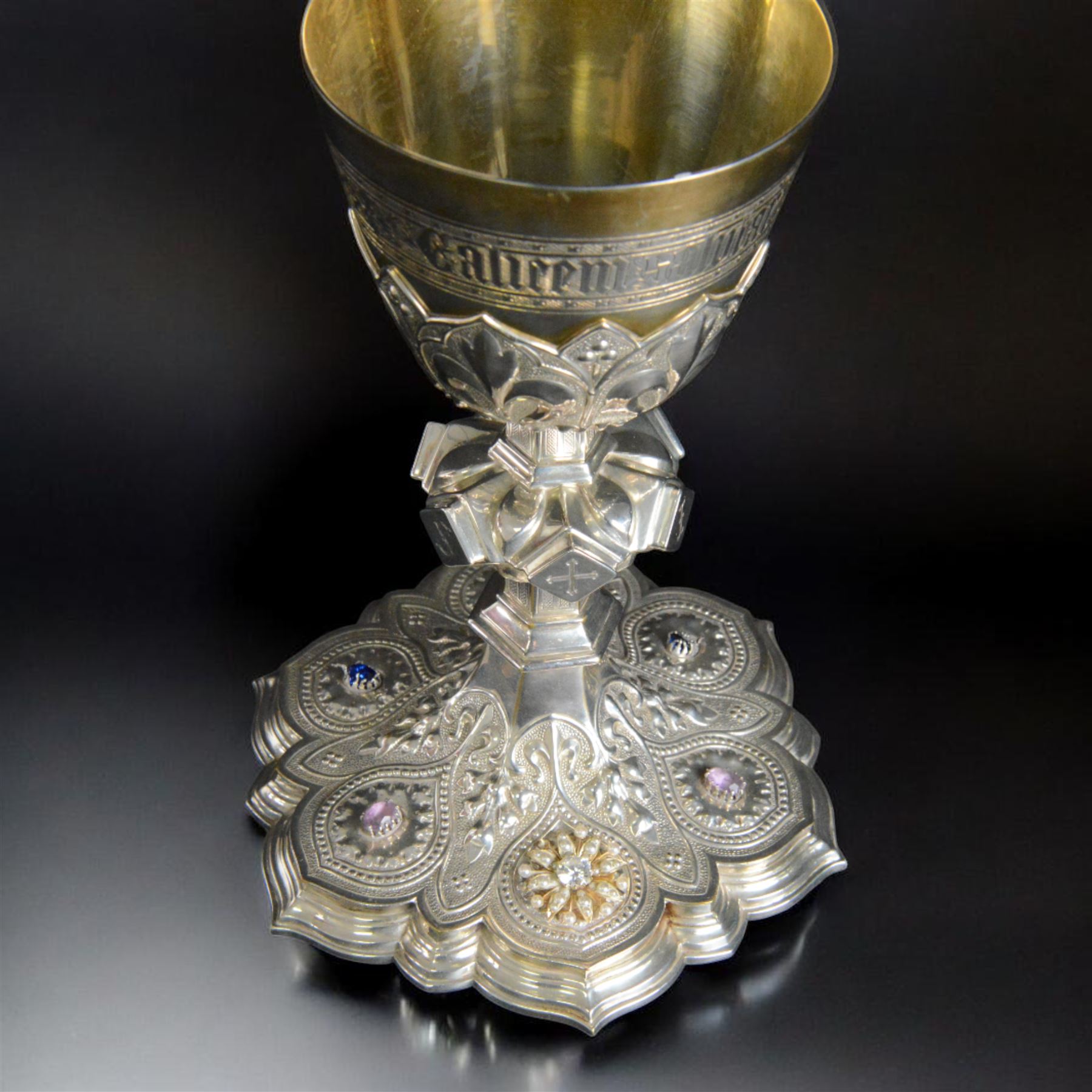 20th Century silver plated Gothic chalice, embossed throughout with fleurs de lis, foliate and bead decoration, on a knopped stem with flared and cusped foot, inset with three amethyst and two blue paste stones and applied paste and split pearl brooch, engraved beneath 'In Memory of my Mother R.I.P ... Aug 15th 1937, H23cm