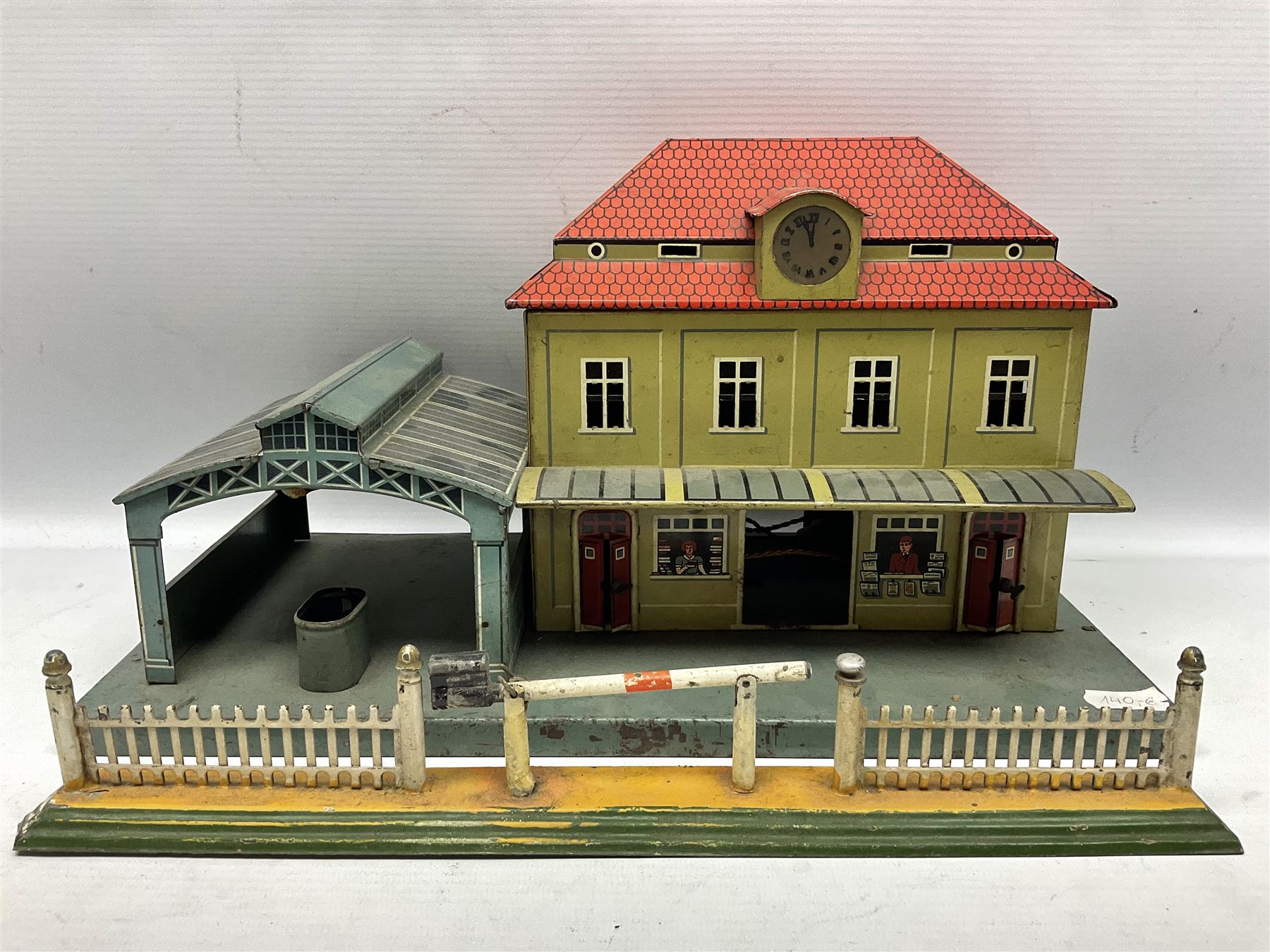 '0' gauge - Bing tin-plate two-storey double sided station with open walk-through to one end, rail side canopy, hinged doors and removable roof giving access to clock illumination L35cm; Bing hand-cranked turntable and open wagon; Marklin tin-plate level crossing barrier and Newspaper vendor's tin-plate four-wheel hand cart (5)