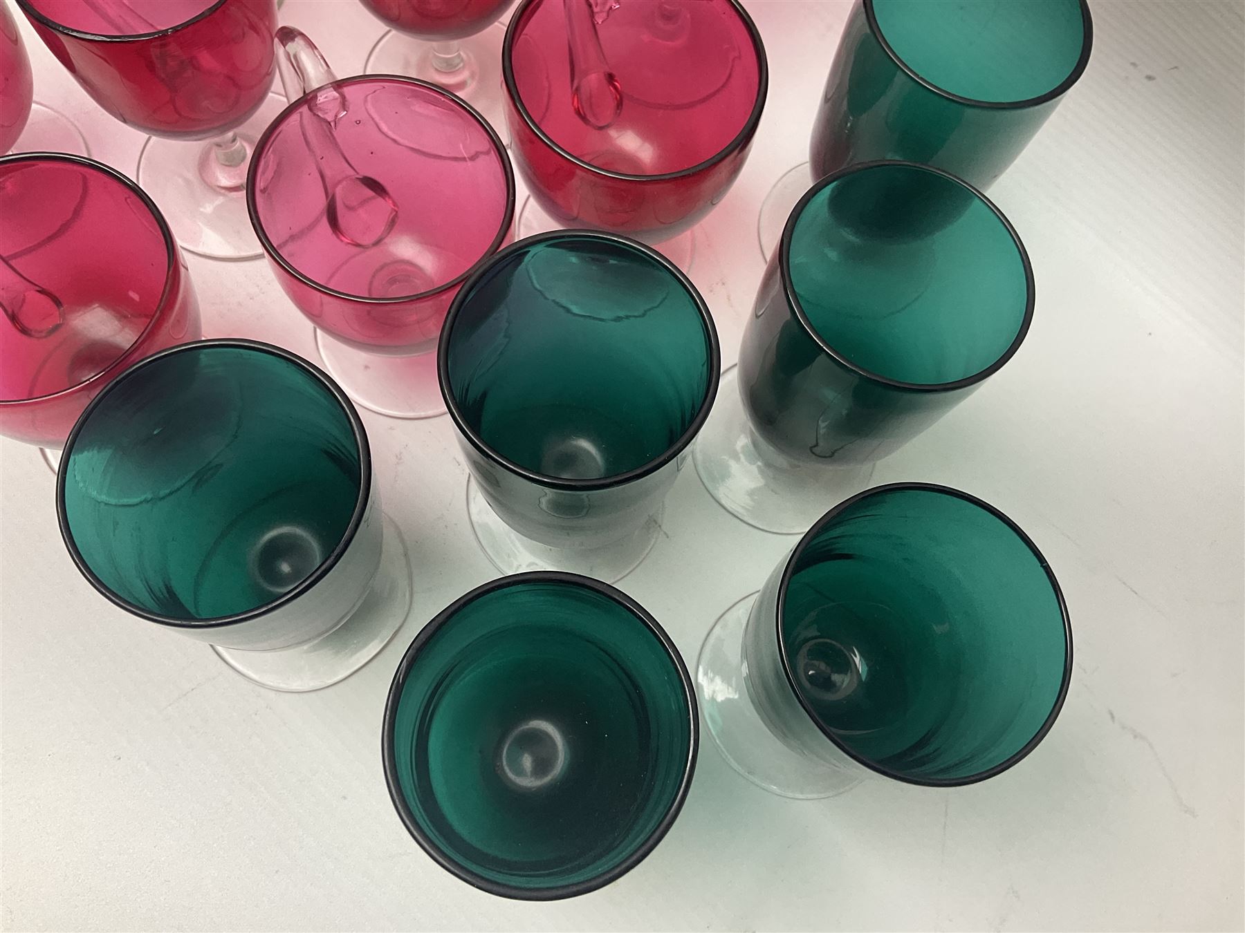 Collection of 19th century coloured glasses, to include nine cranberry glass punch cups, each with clear glass handle and foot and a set of six green glasses, with short clear stems, tallest H10cm