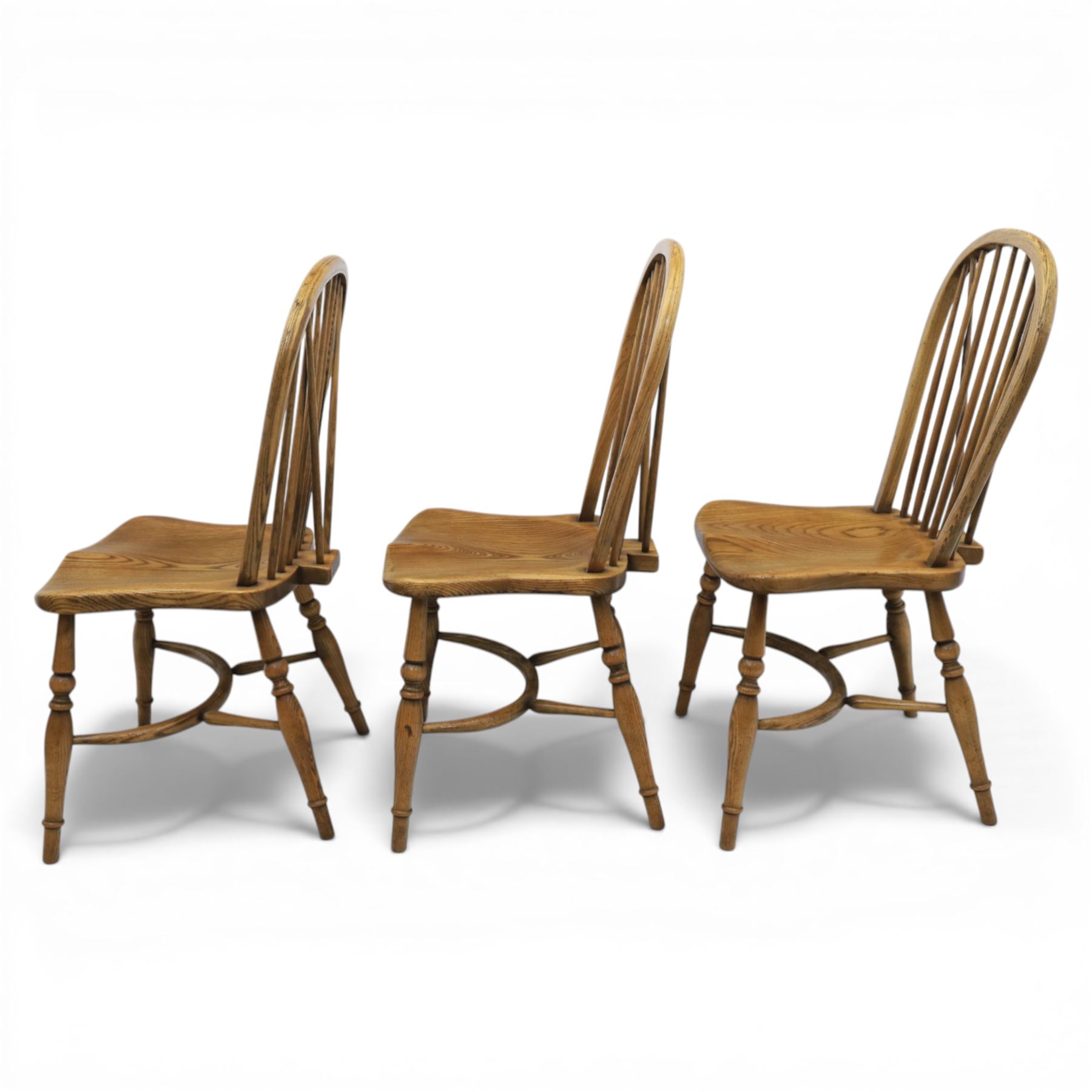 Traditional elm and beech Windsor dining chairs, each with hoop back and turned spindles over a shaped solid seat fitted with loose floral upholstered cushions, raised on turned tapering supports united by crinoline stretchers