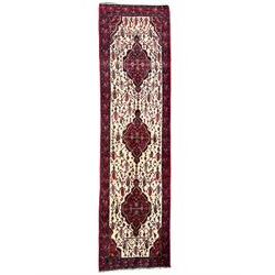 North West Persian Saveh crimson ground runner rug, the three lozenge pole medallions in an ivory field, surrounded by stylised plant motifs, the guarded border decorated with repeating geometric patterns