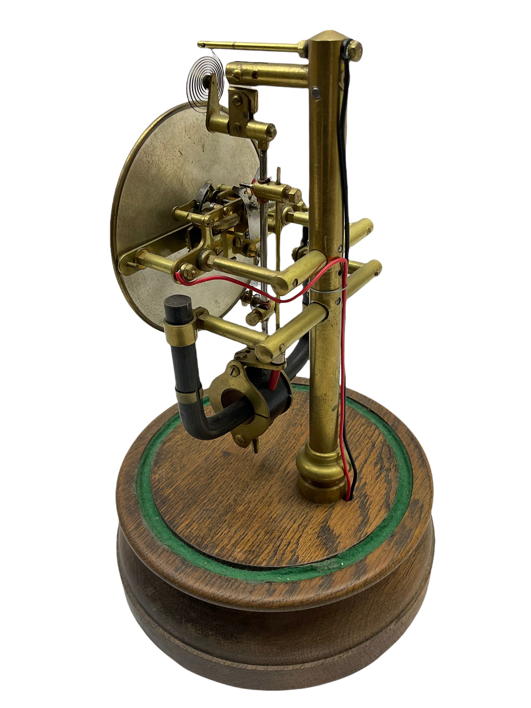 A 1920’s French 800-day Bulle electric battery clock on a turned wooden base, with a circular silvered dial with Arabic numerals, minute track and steel spade hands, skeletonised brass movement and escapement, the magnetic pendulum action is activated by the battery power source located in the base of the clock. No Dome.