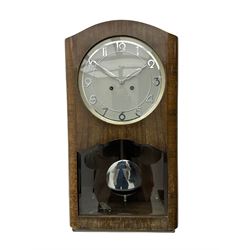 A mid 20th century German wall clock in a veneered mahogany case with a German eight day “Kienzle” movement sounding the hours and half hours on twin gong rods, 9” circular dial with chrome Arabic numerals and pierced baton hands,  full length door with glazed dial and pendulum apertures, chrome pendulum bob. 
 


