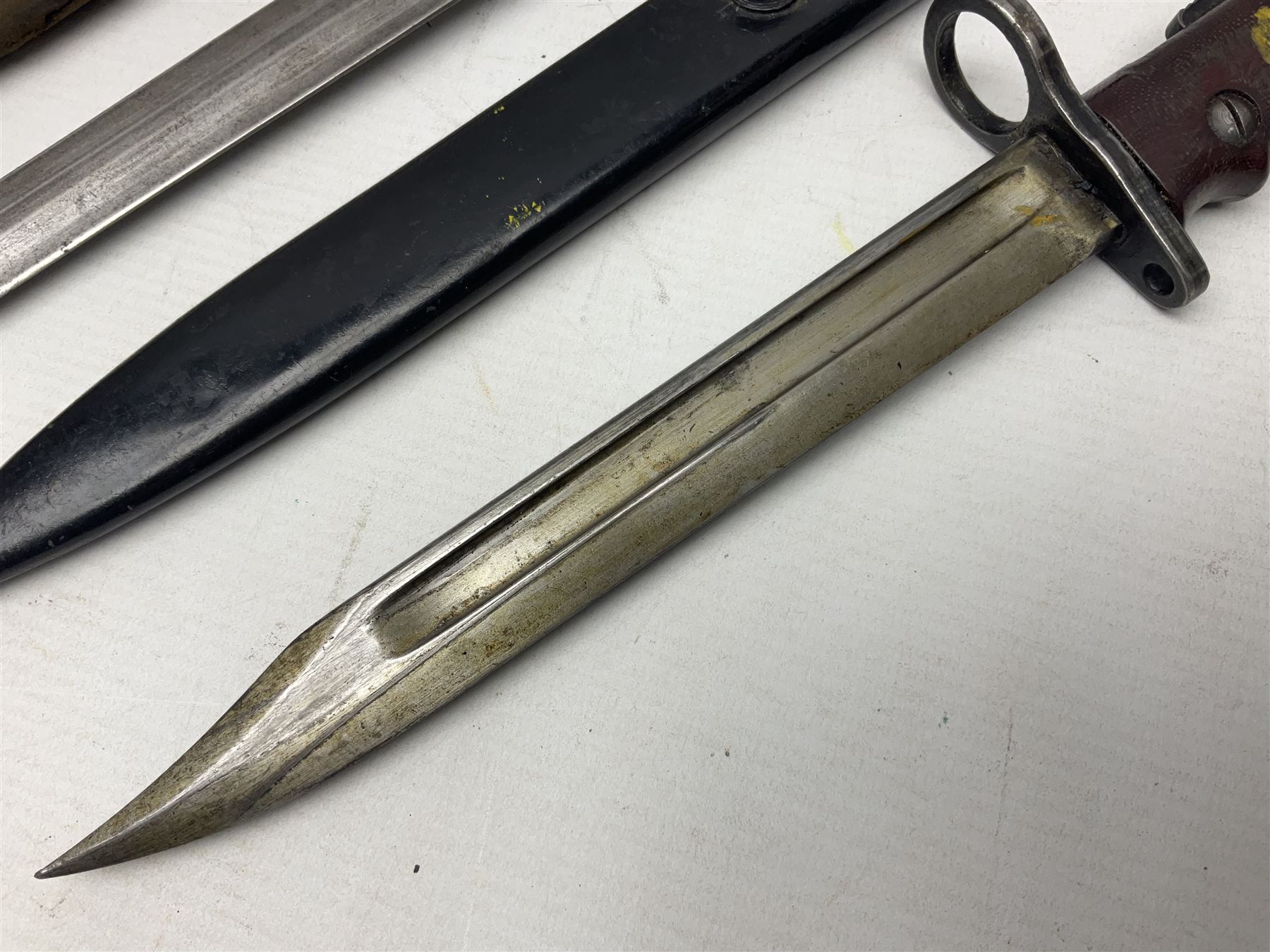 British No 7 MKI knife bayonet with 20cm single edged fullered clipped point blade;  blackened steel, large muzzle ring cross-guard; blackened swivelling pommel marked 'F5H'; red Tufnol composite grips; in blackened steel scabbard L33cm overall; British Pattern 1888 bayonet with scabbard; and German Ersatz bayonet with scabbard (3)