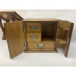 Early 20th century oak smokers cabinet, with brass shield shaped mounts, opening to reveal a compartmentalised interior with three drawers, pipe rack and tobacco jar, together with a small wooden shelf, smokers cabinet H28.5cm