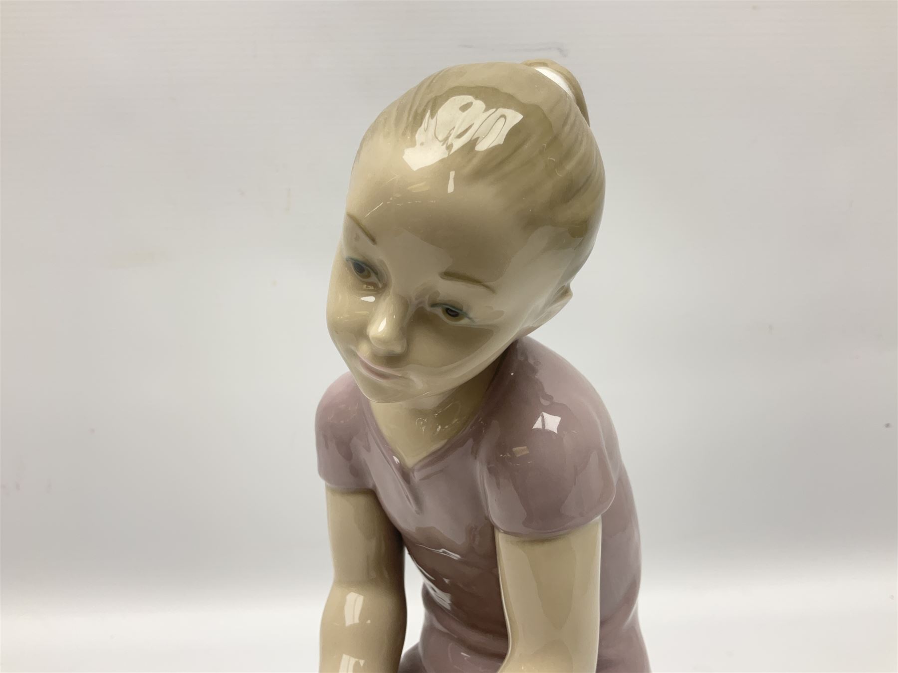 Large Nao figure modelled as a young girl seated upon a rock holding a rose, H30cm