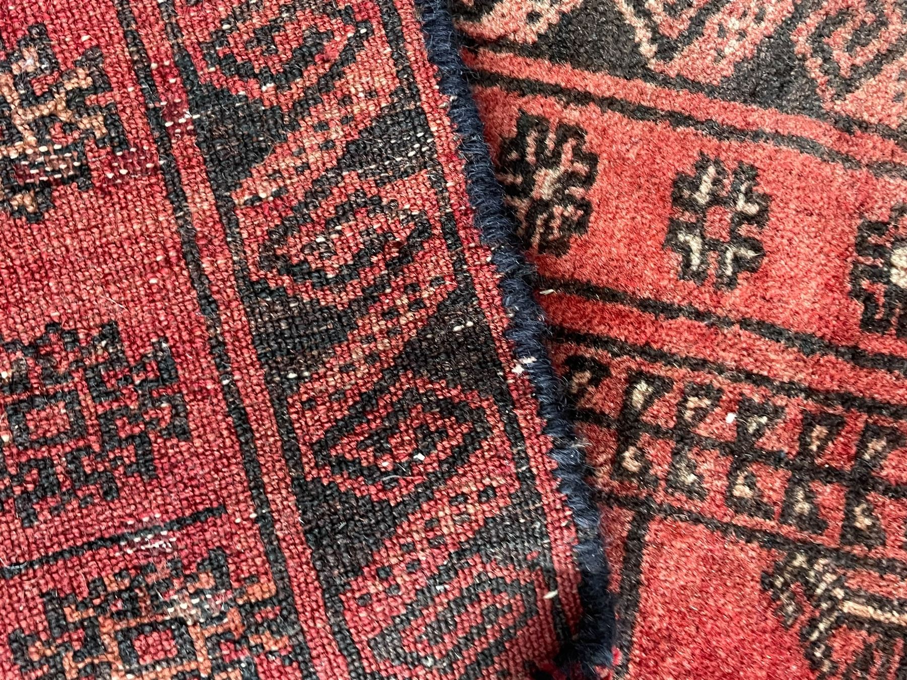 Afghan Bokhara red ground rug, the field decorated with three rows of Gul motifs, within multiple band borders decorated with trailing hook and geometric motifs 