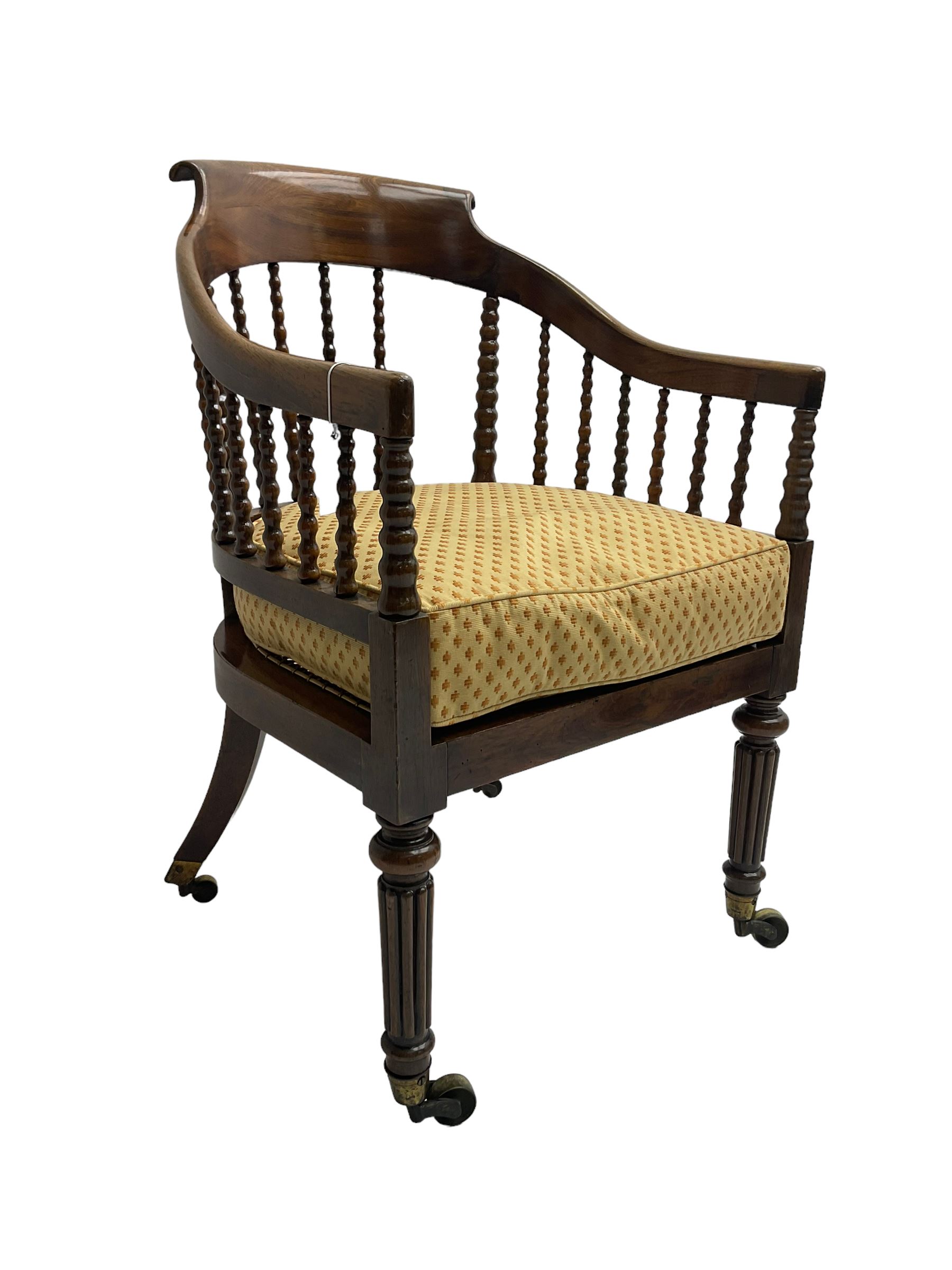William IV rosewood tub armchair, the arched bow cresting rail over graduated bobbin turned spindles, cane seat with loose cushion, terminating in brass cups and castors.