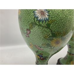Pair of cloisonné lidded vases of baluster form decorated with blooming branches of flowers upon patterned green ground, together with further pair of cloisonne vases decorated with birds and butterflies amongst peonies and cherry blossom upon patterned lilac ground, all with wood bases, tallest H31cm