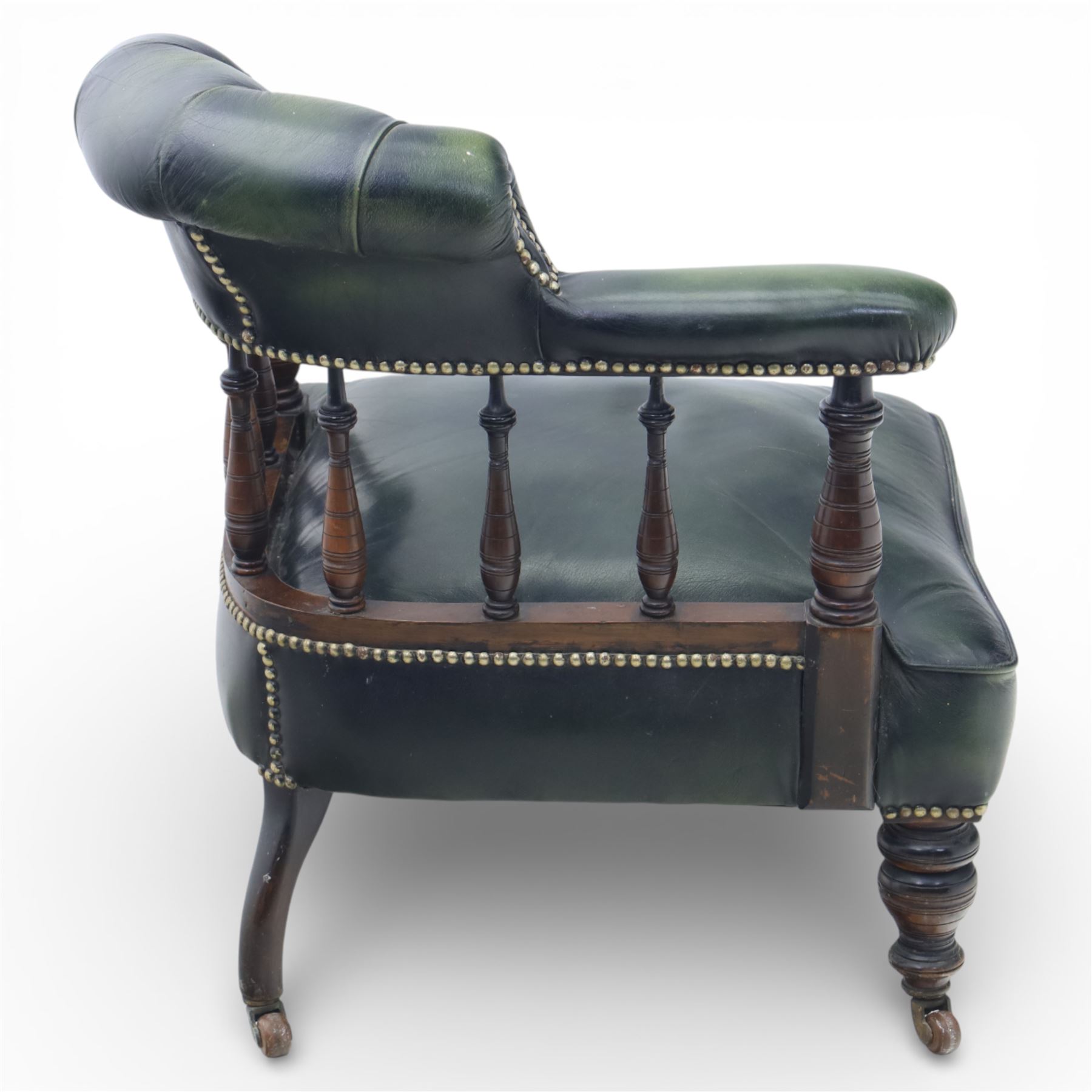 19th century green leather upholstered corner chair, with deep buttoned back and swept padded arms with close studded borders, raised on turned supports united by turned spindles, terminating in brass castors