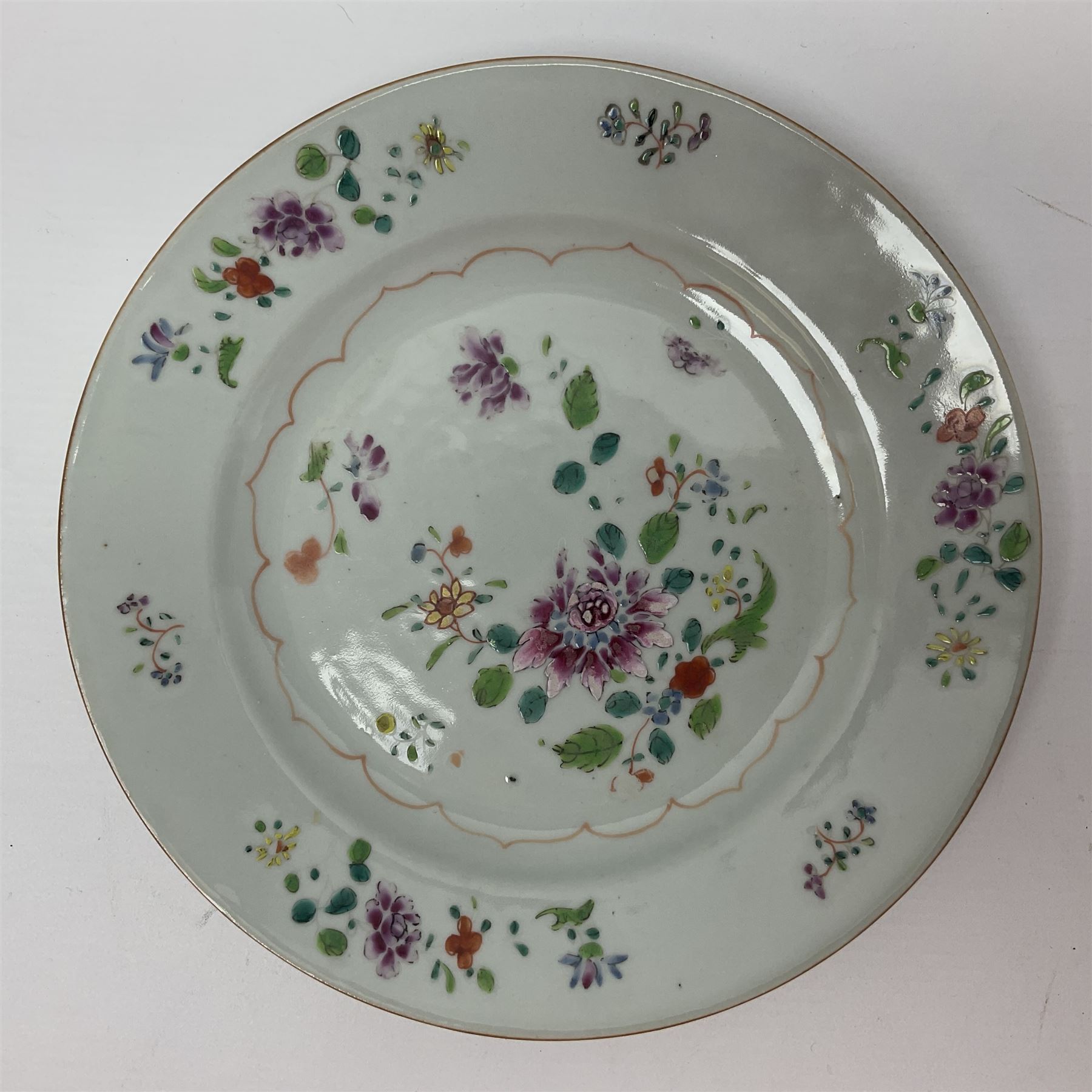 Three 18th century Chinese Famille Rose plates, the first example enamelled with blossoming peonies, rockwork and fence, the other two examples of similar design, decorated with blossoming peonies and sprigs within shaped inner borders, each approximately D23cm