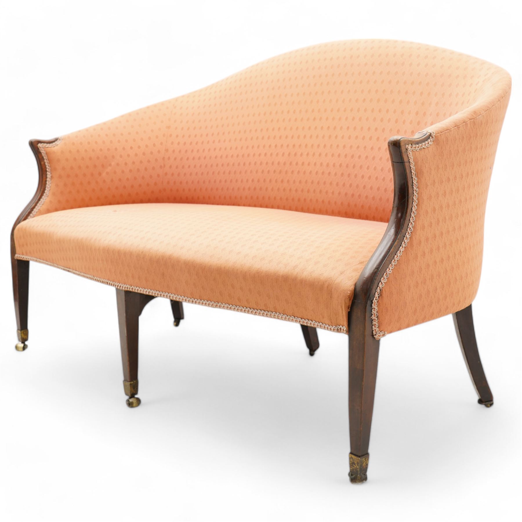 George III Hepplewhite design settee, arched back over serpentine set, upholstered in salmon fabric with repeating pattern, on square tapering supports with brass cups and castors 