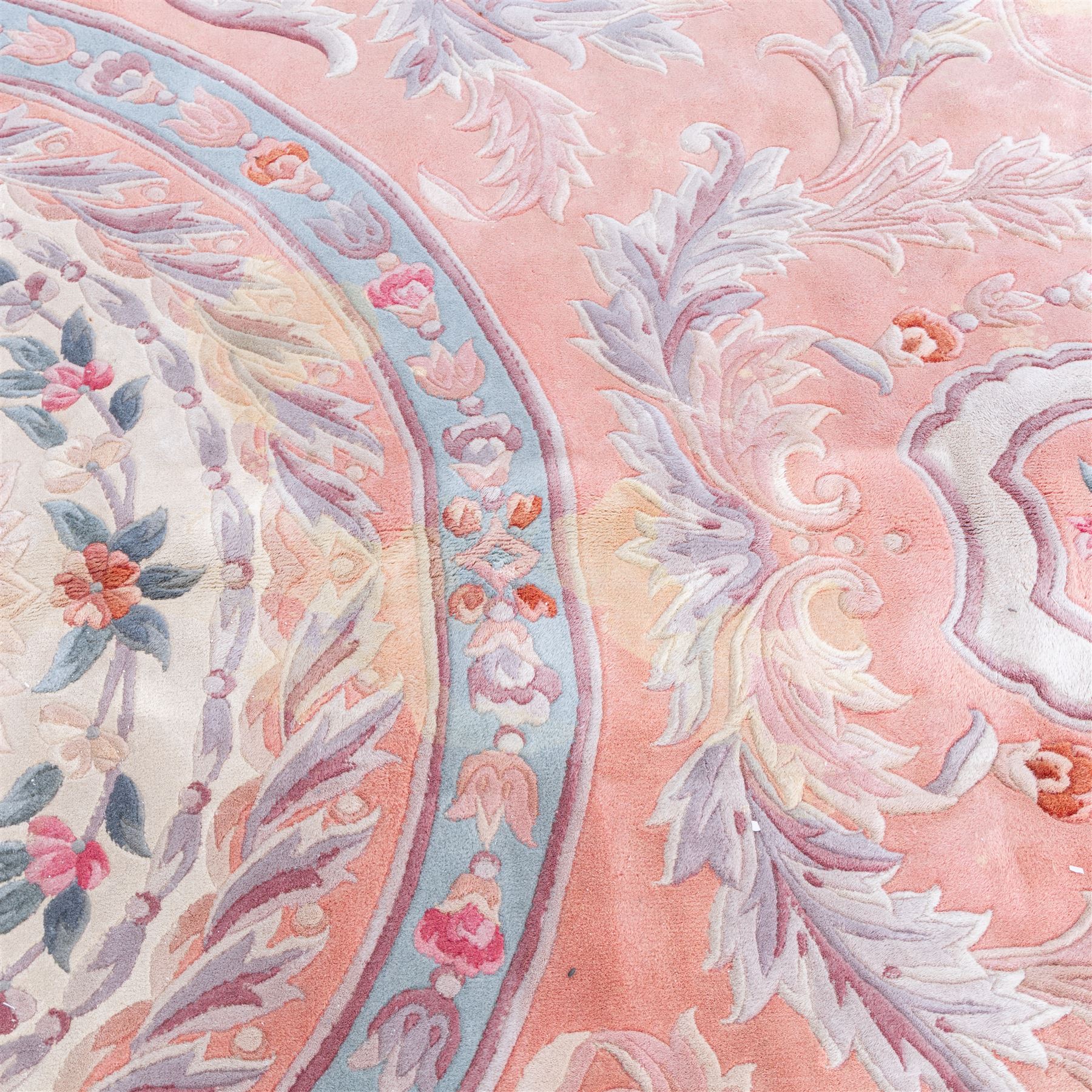 Large late 20th century Aubusson style wool carpet, peach and pastel toned field with central floral medallion enclosing scrolling acanthus and and foliate sprays, surrounding field decorated with further stylized foliage and and floral ornament, within shaped reserves and indigo corner spandrels, enclosed by narrow guard border, cotton fringe ends