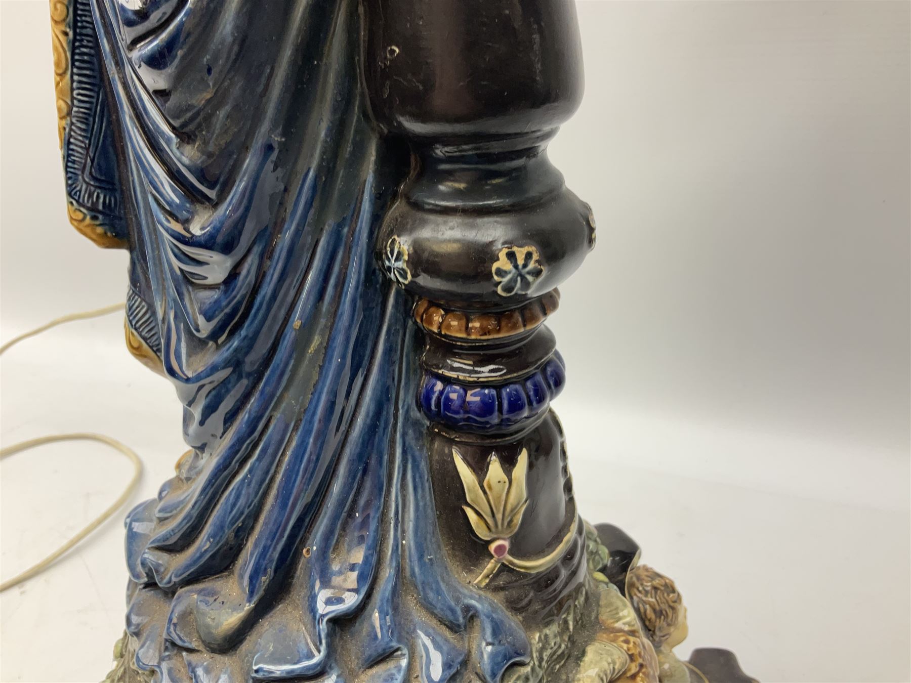 Composite table lamp modelled as a Roman Emperor donning blue robes, upon quatrefoil base modelled with rams heads and winged cherubs, H56cm excl fitting