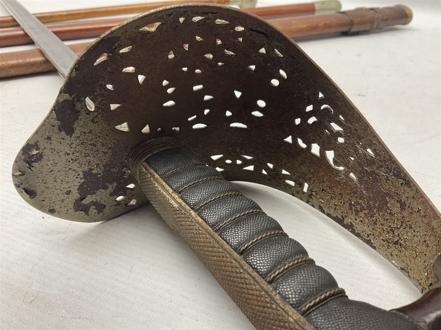 George V 1897 pattern Army Officer's sword by Henry Wilkinson Pall Mall London, the 82.5cm 'London Made' blade etched to both sides with Royal Crests and cyphers etc, pierced half-basket hilt with wire-bound fish skin grip and remains of leather knot strap; in leather covered field service scabbard L101cm overall; and two 14th Prince of Wales Own swagger sticks (3)