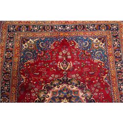Persian Kashan hand-knotted rug, madder red ground centred by circular floral medallion with pendants, surrounded by scrolling vines, palmettes and flowerheads, dark navy spandrels, enclosed by dark navy floral border with multiple guard stripes