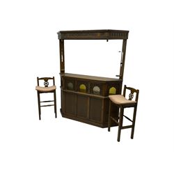Old Charm - oak corner bar, the canopy frieze carved with scrolls, front decorated with arched apertures glazed with bullseye and mottled glass panes, skirted base, together with two bar stools