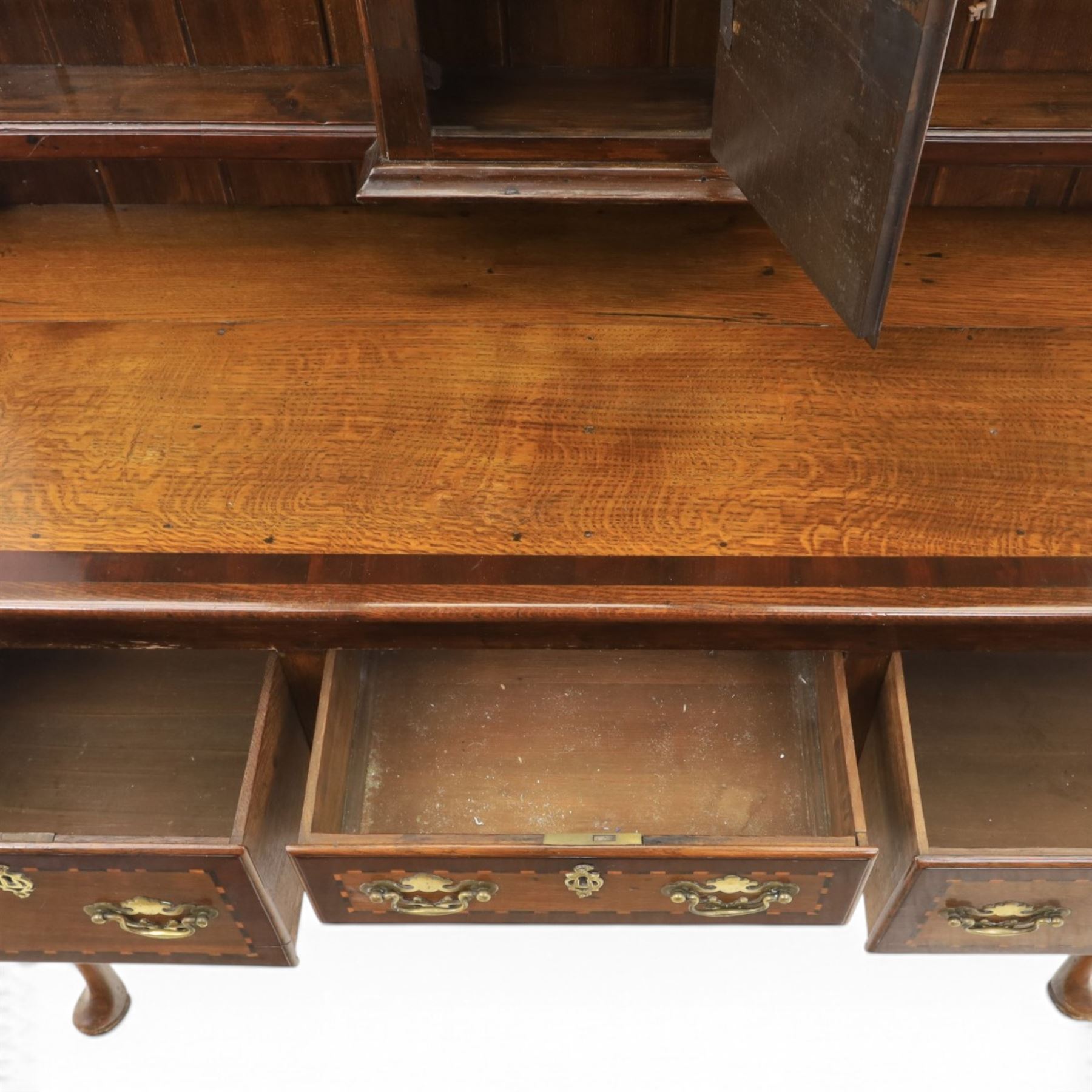 Late 19th century inlaid oak dresser and plate rack, plate rack with projecting cornice and fretwork, with three shaped shelves for plates, central cupboard with inlaid shell and border, brass escutcheon and key, the lower section with crossabanded top, above three drawers with brass handles and inlaid border, shaped apron raised on cabriole supports 