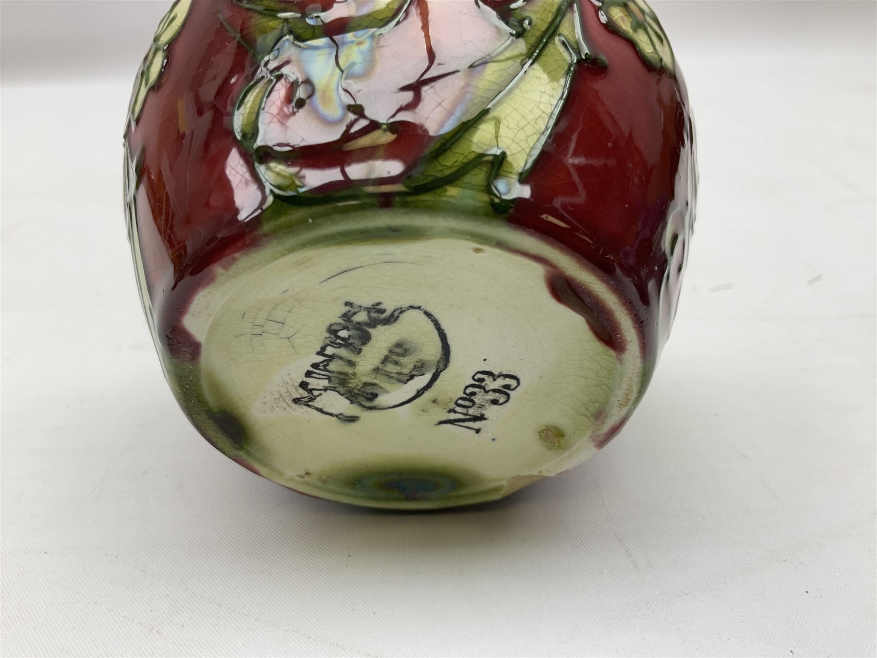 Three Minton Secessionist vases, with tube-lined stylised flower decoration, two upon a red ground and third upon a purple ground, all with printed mark to base 'Minton Ltd, No. 33', H13cm