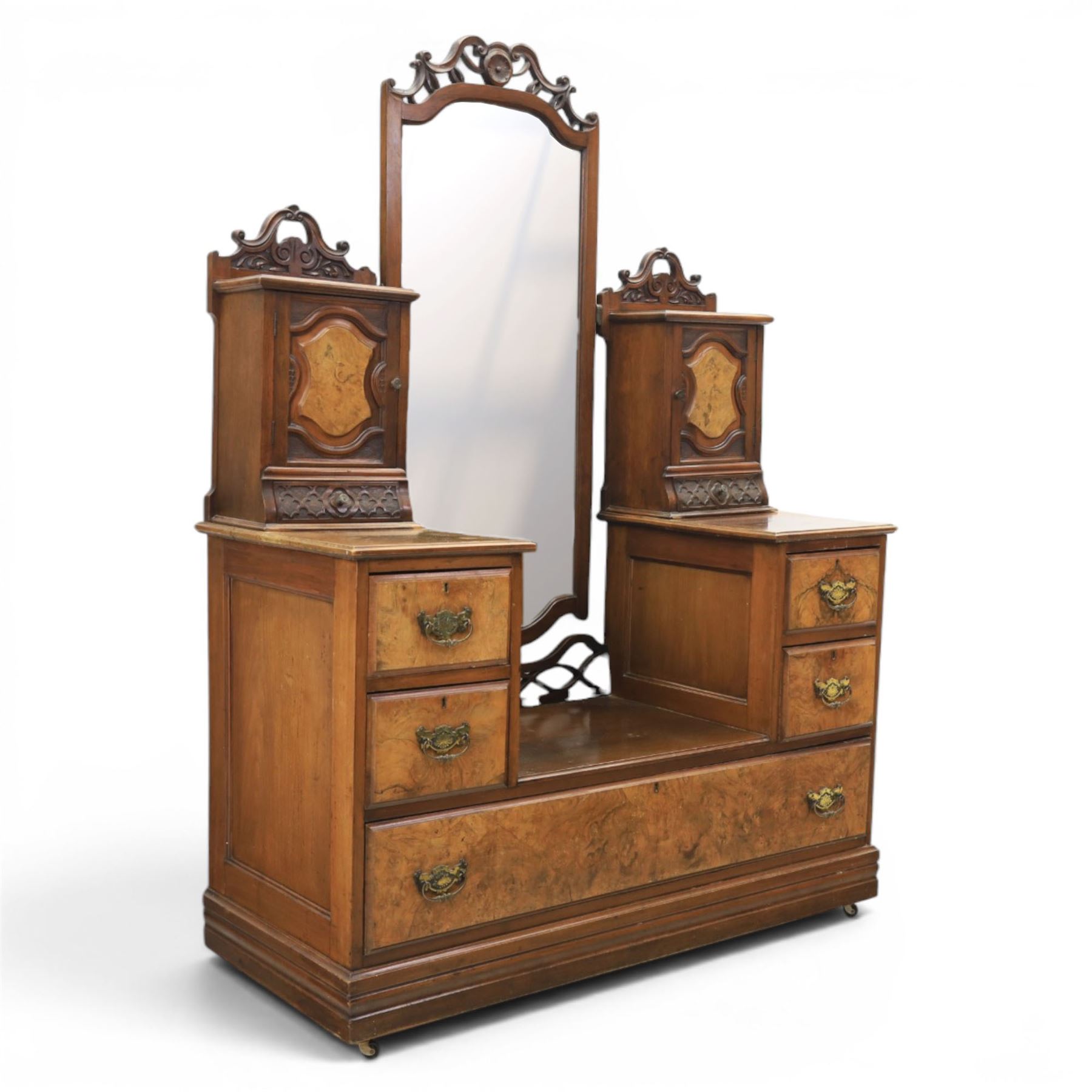 Edwardian figured walnut dressing chest, with central tilting mirror with pierced fret work, flanked by cabinet with figured walnut panelled door above a trinket drawer, with four short over a long long drawer, raised on a plinth base with castors 