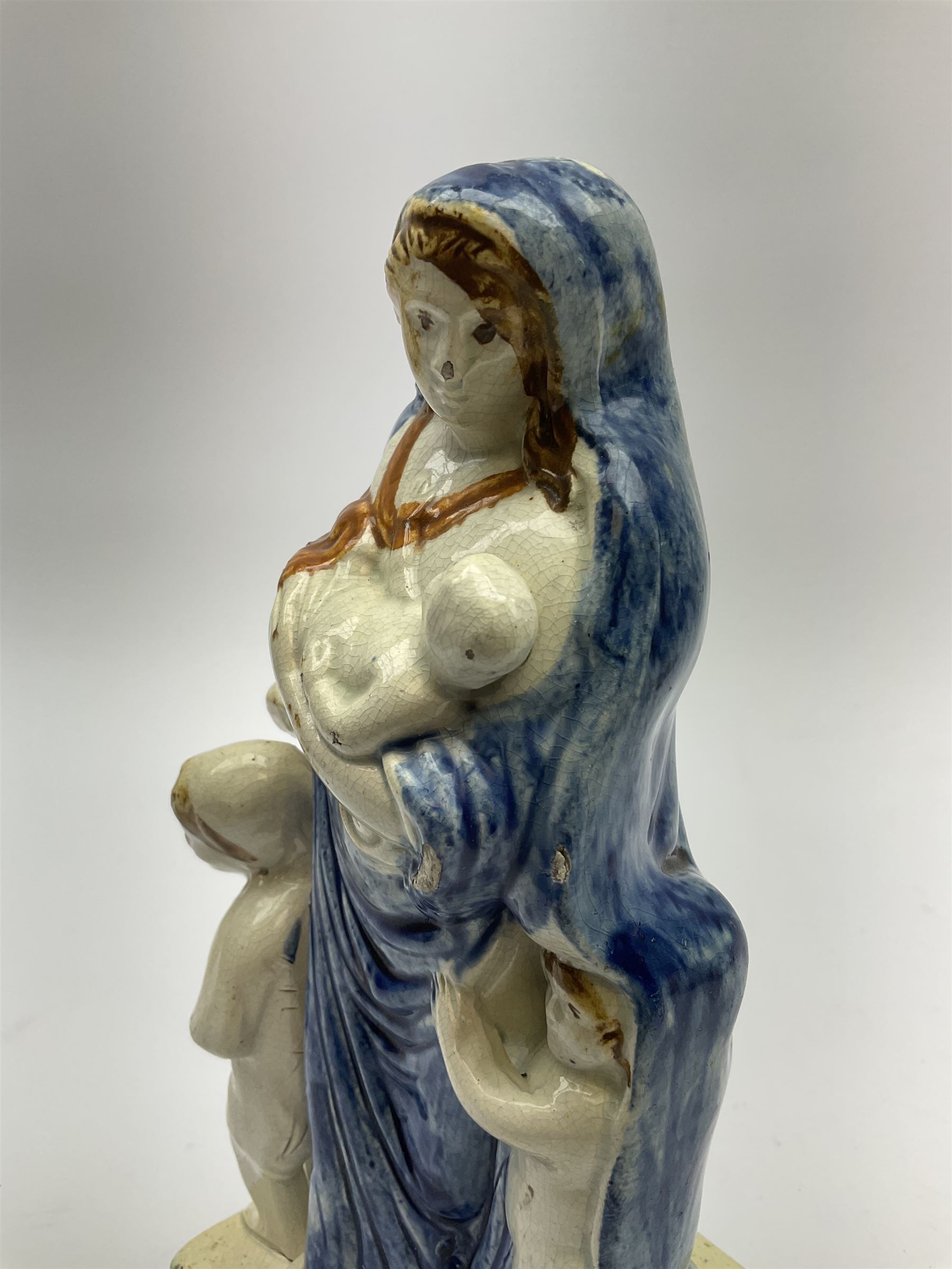 Late 18th century Prattware figure representing Charity, modelled as a mother with baby in her arms and two small children clutching at her robes, upon a square base, overall H21cm.