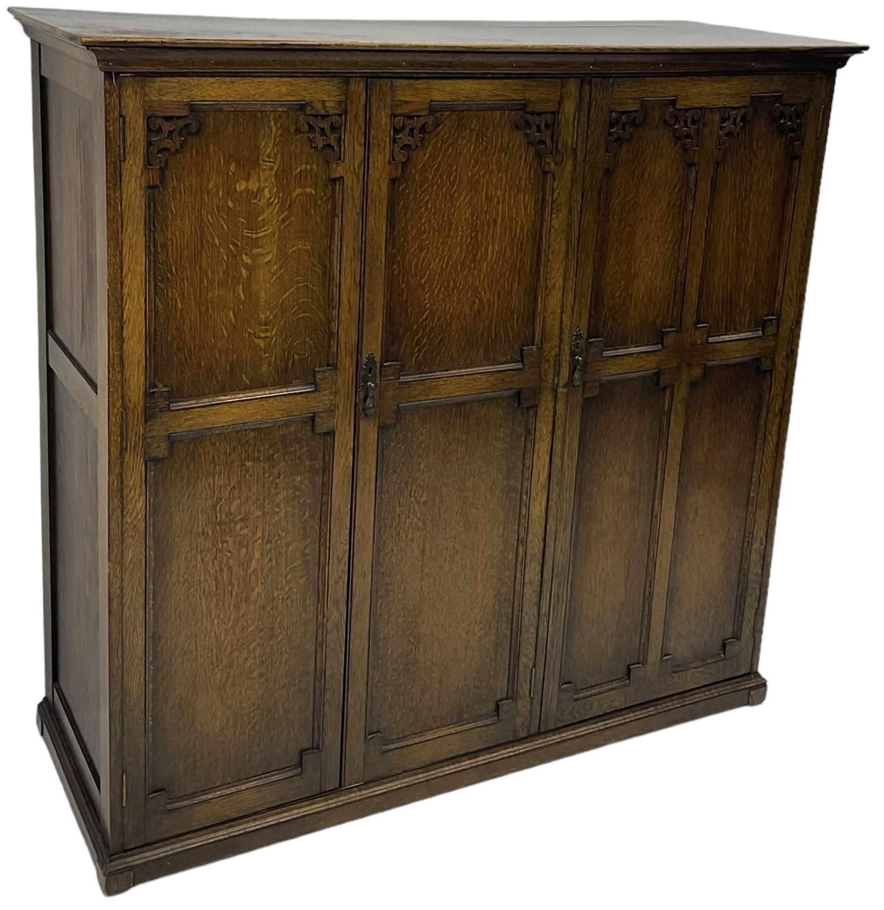 Early 20th century oak triple wardrobe, three panelled doors with geometric mouldings and fretwork spandrels, the interior fitted with slides and hanging rail